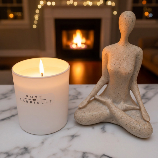 Lit white candle beside a seated sculpture on marble, with a fireplace in the background.